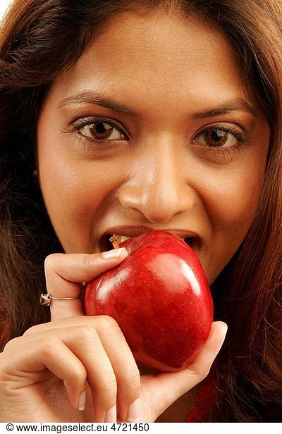 South Asian Indian teenager girl wearing red colour contact lenses in eyes eating red apple as fruit good for health MR686G