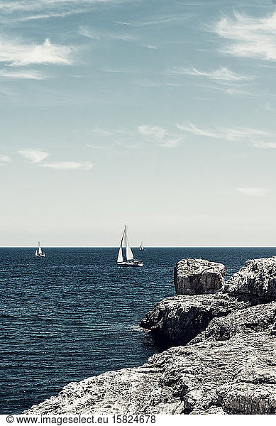 Spain  Balearic Islands  Santanyi  Rocky shore of Mediterranean Sea with sailboats sailing in background