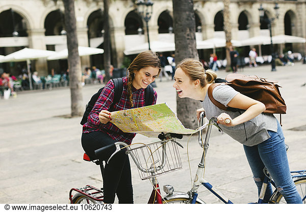 Spain  Barcelona  two happy young women with map on bicycles in the city