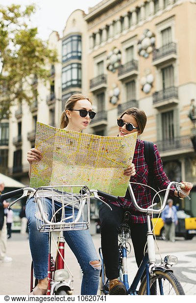 Spain  Barcelona  two young women with map on bicycles in the city