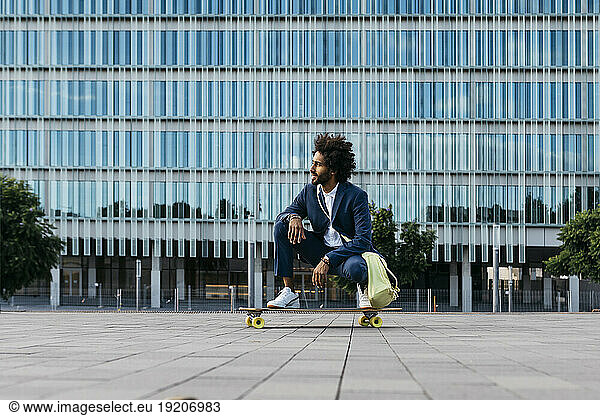 Spain  Barcelona  young businessman crouching on skateboard in the city