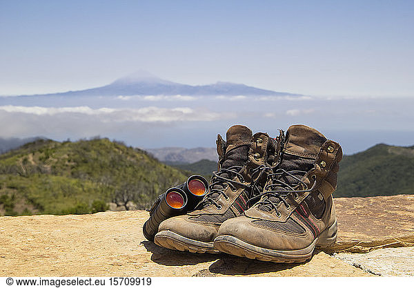Spain  Canary Islands  La Gomera  Binoculars and pair of brown hiking boots lying at summit of Garajonay with Teide volcano looming in distant background