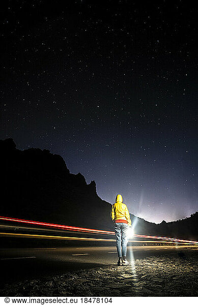 Spain  Canary Islands  Vehicle light trails passing woman standing on roadside in El Teide National Park