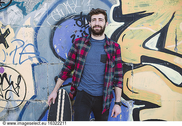 Spain  La Coruna  portrait of hipster leaning against wall with his longboard