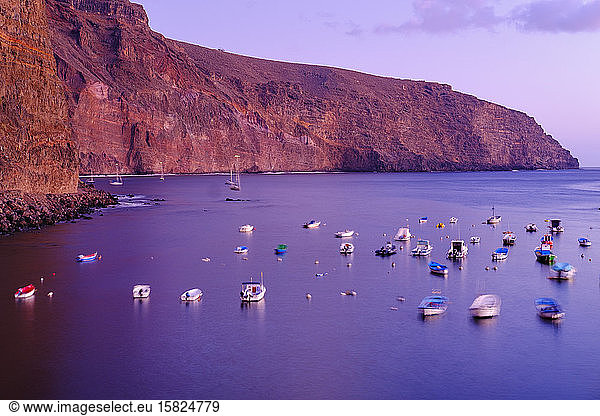 Spain  La Gomera  Valle Gran Rey  Boats moored in front of coastal cliff at purple dusk