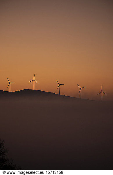 Spain  Province of Cadiz  Tarifa  Silhouettes of wind turbines standing against moody sky at foggy dawn