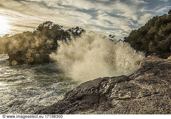 Spanien  Mallorca  Meereswelle schlägt gegen Felsen am Strand Cala des Moro bei Sonnenuntergang