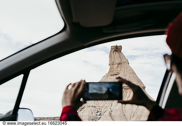 Spanien  Navarra  Junge Frau sitzt im Auto und macht Smartphone-Fotos von Sandstein-Felsformation in Bardenas Reales