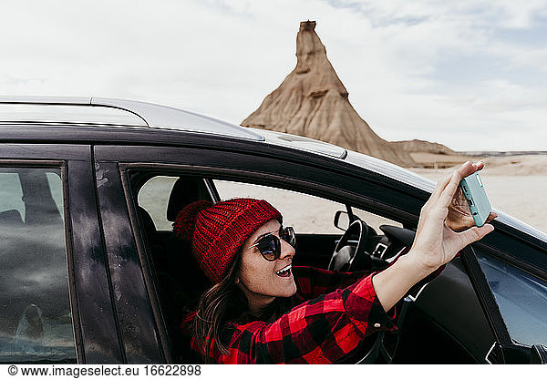 Spanien  Navarra  Touristin lehnt sich aus dem Autofenster und macht Smartphone-Fotos von Bardenas Reales