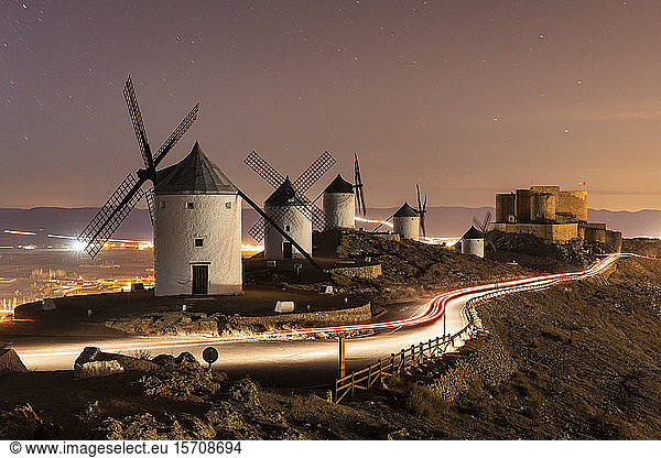Spanien  Provinz Toledo  Consuegra  Fahrzeugschleifen vor einer Reihe alter Windmühlen  die nachts auf einem Hügel stehen