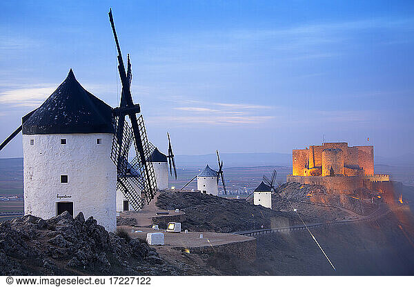 Spanien  Provinz Toledo  Consuegra  Historische Windmühlen in der Abenddämmerung mit der Burg von La Muela im Hintergrund