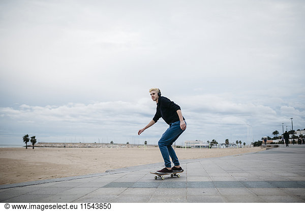 Spanien  Torredembarra  junger Skateboarder beim Musikhören mit Kopfhörern