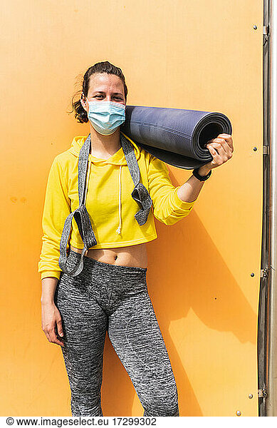 Spanische Frau mit Sportmatte und Schutzmaske posiert