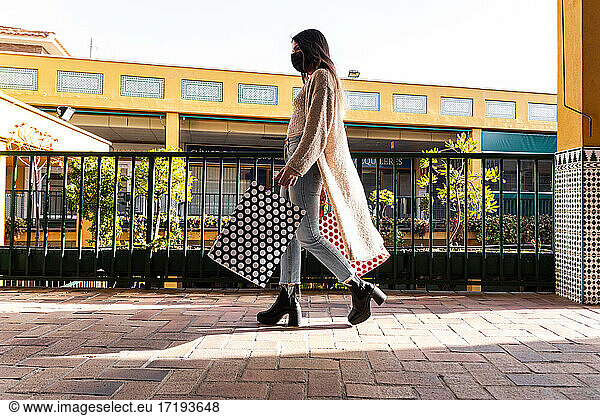 Spanish brunette girl with face mask walking with shopping bags in a shopping mall.