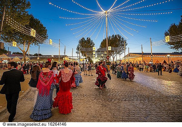 Spanish woman with colourful flamenco dresses  illuminated decorated street  evening mood  Feria de Abril  Sevilla  Andalusia  Spain  Europe