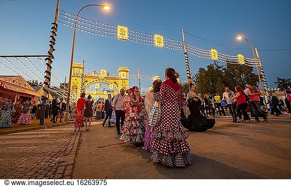 Spanish women with flamenco dresses in front of the illuminated Portada  entrance gate  Feria de Abril  Sevilla  Andalusia  Spain  Europe