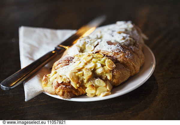 Specialist coffee shop. A fresh pastry  an almond croissant on a place with a knife.