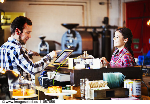 Specialist coffee shop. A man behind the counter using a touch screen to record transactions  and a woman customer.