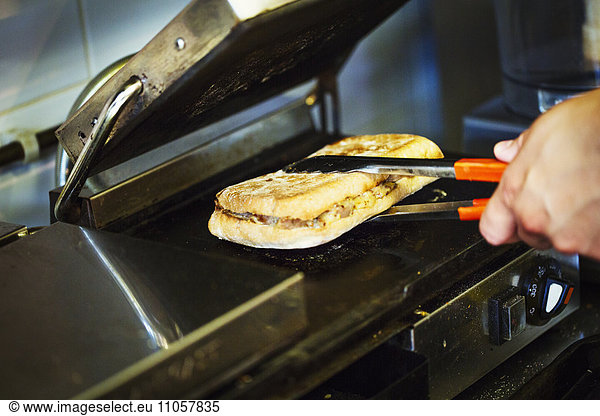 Specialist coffee shop. A person preparing a toasted sandwich at a grill.