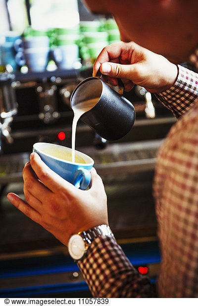 Spezialisiertes Kaffeehaus. Eine Person  die Kaffee kocht und Milch in eine schräg gehaltene Tasse gießt.