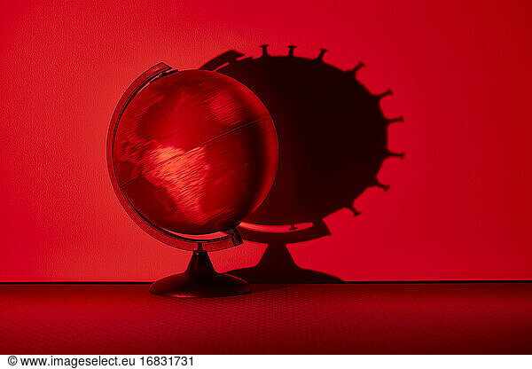 Spinning globe casting coronavirus biological cell shadow on red wall