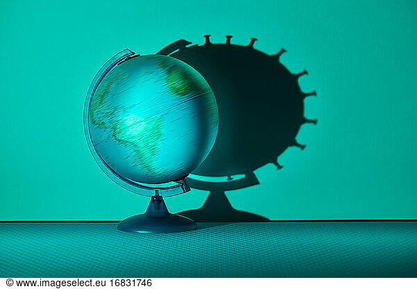 Spinning globe casting coronavirus biological cell shadow on wall