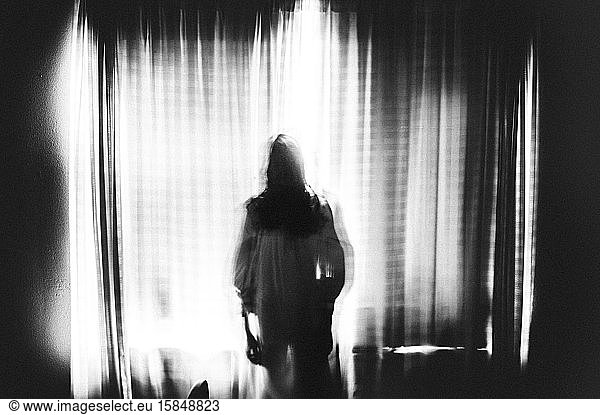 Spooky image of ghost girl standing in window in eery light
