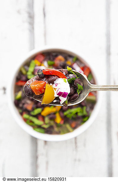 Spoon of black bean soup with bell pepper  cilantro  sour cream and red onions