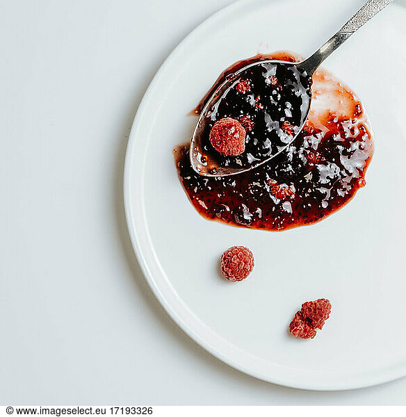 Spoon of raspberry jam on a white plate with frozen berries