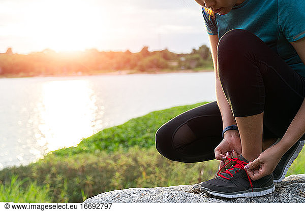 Sport Frau bindet Schnürsenkel vor dem Laufen  Sonnenuntergang auf dem Fluß