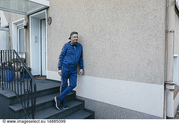 Sportive senior man in tracksuit leaning against house wall