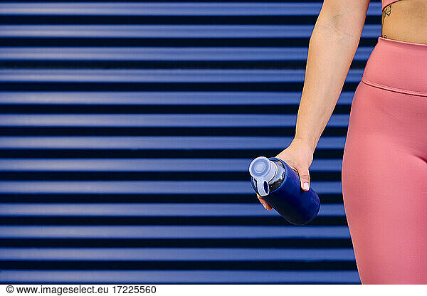Sportlerin hält blaue Wasserflasche vor einer Wand