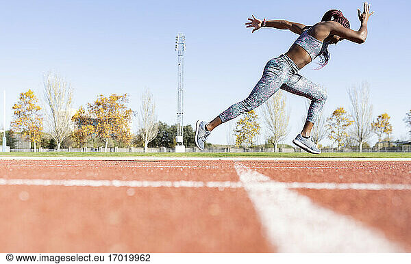 Sportlerin mit Hingabe läuft auf Sportbahn gegen klaren Himmel während sonnigen Tag