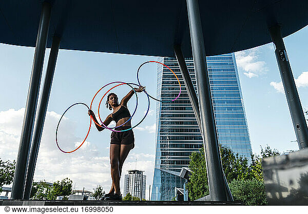 Sportliche Frau balanciert Plastikreifen in moderner Stadt