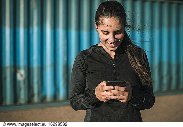 Sportliche Frau benutzt Smartphone im Industriegebiet