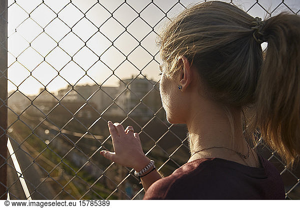 Sportliche junge Frau schaut durch einen Zaun