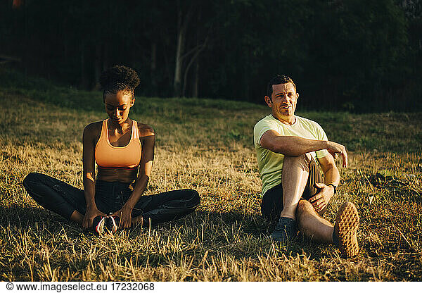 Sportsman and sportswoman doing relaxation exercise while sitting on grassy area