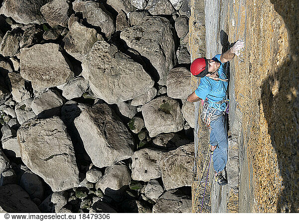 Sportsman climbing rocky wall on sunny day