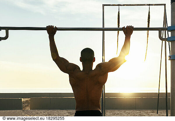 Sportsman exercising on gymnastics bar on sunny day