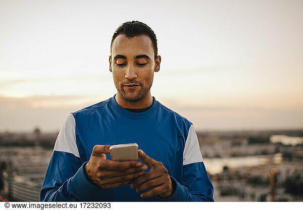 Sportsman using smart phone against sky during sunset