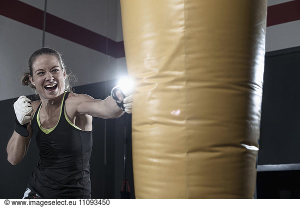 Sportswoman doing strength training by punching on punch bag in the gym