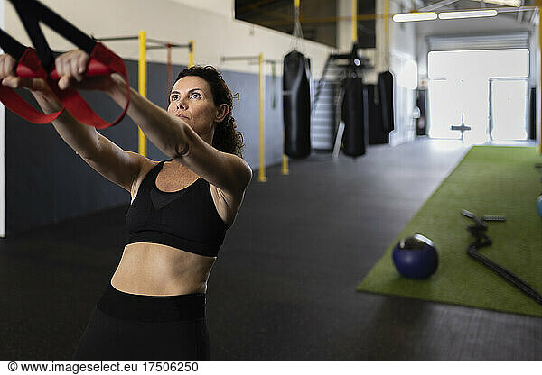 Sportswoman leaning backwards pulling straps in gym