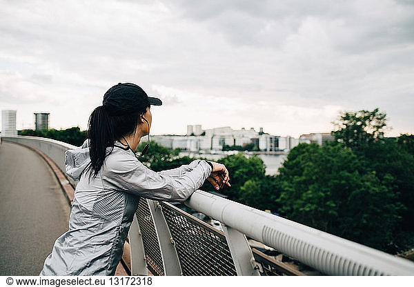 Sportswoman leaning on railing at footbridge in city