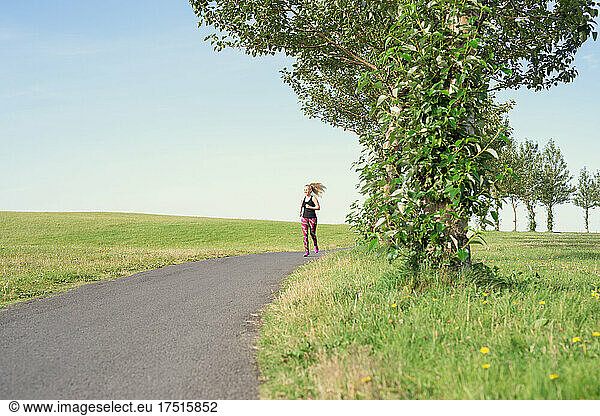 Sportswoman running on road amidst grassy fields