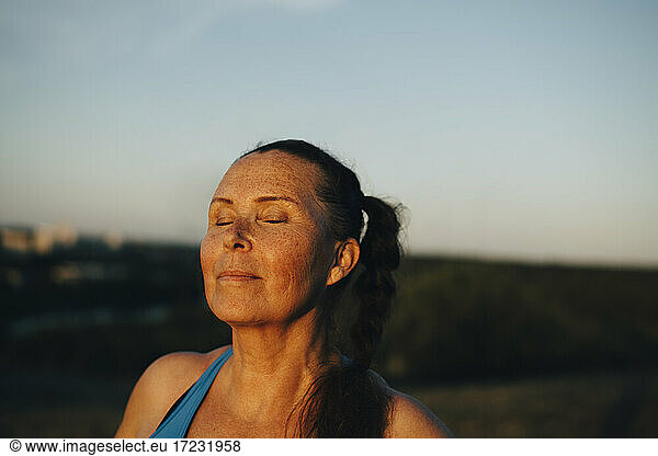 Sportswoman with eyes closed against sky during sunset