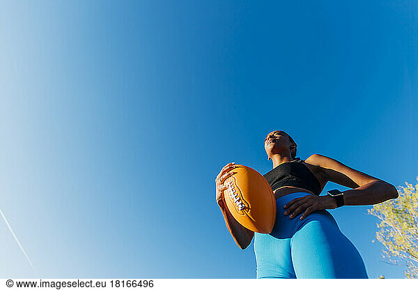 Sportswoman with hand on hip holding American football