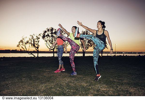 Sportswomen exercising on field against clear sky at park during sunset