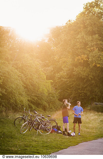 Sporty male friends standing by bicycles at park during sunset
