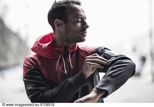 Sporty man adjusting arm band while listening to music