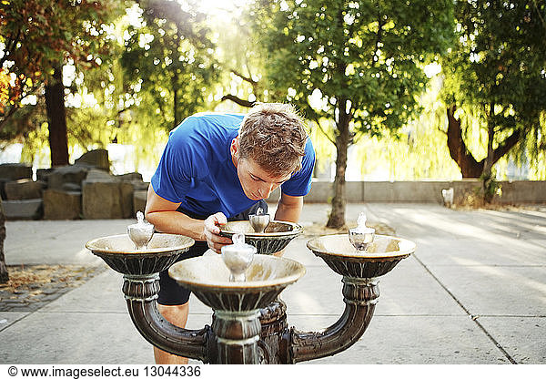 Sporty man bending over drinking fountain on footpath